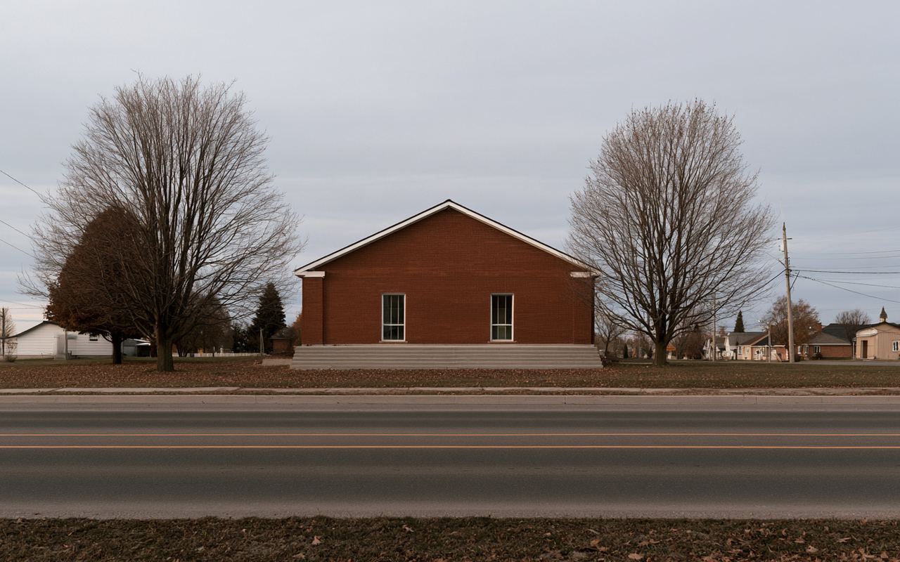 A single-storey red brick community hall set back from a village road, bare maples on either side, under a flat grey autumn sky.